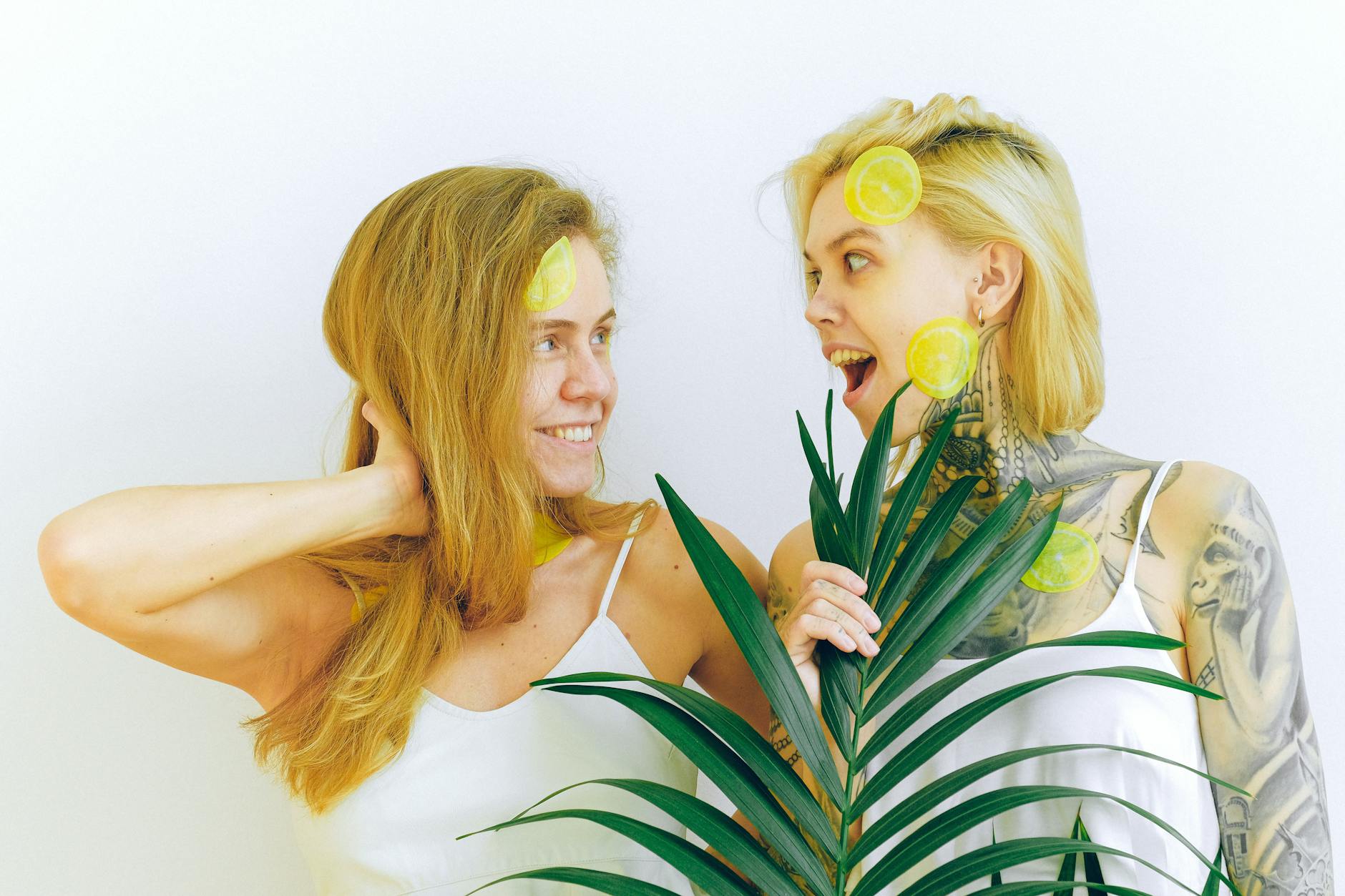 Two women smiling indoors with lemons and tropical plants, expressing joy and celebration