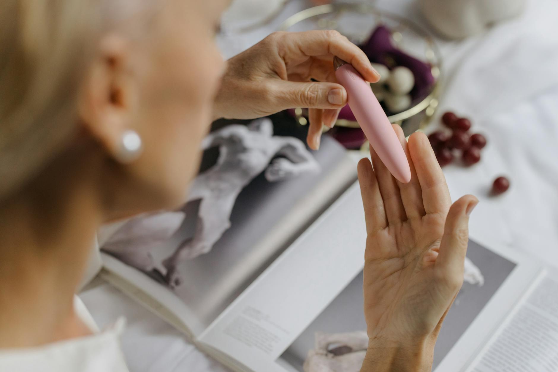 Close-up of a woman holding a lemon clitoral vibrator, surrounded by intimate personal items and art books.